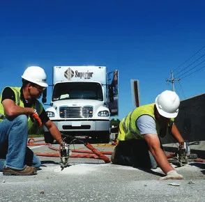 Workers repairing road with machinery near truck.