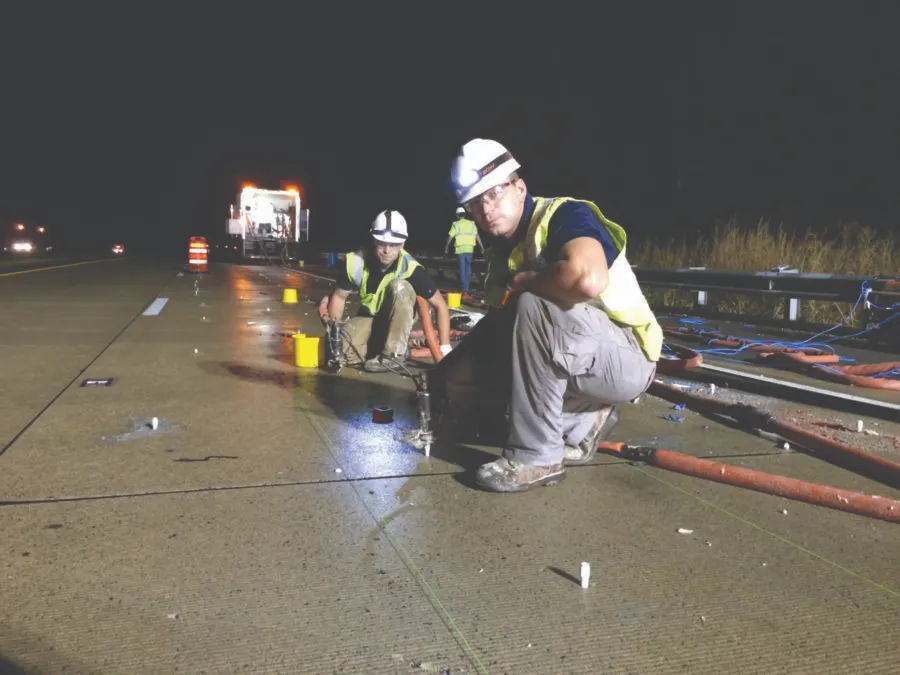 Workers repairing highway at night under bright lights.