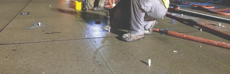 Worker kneeling on concrete floor injecting concrete lifting material