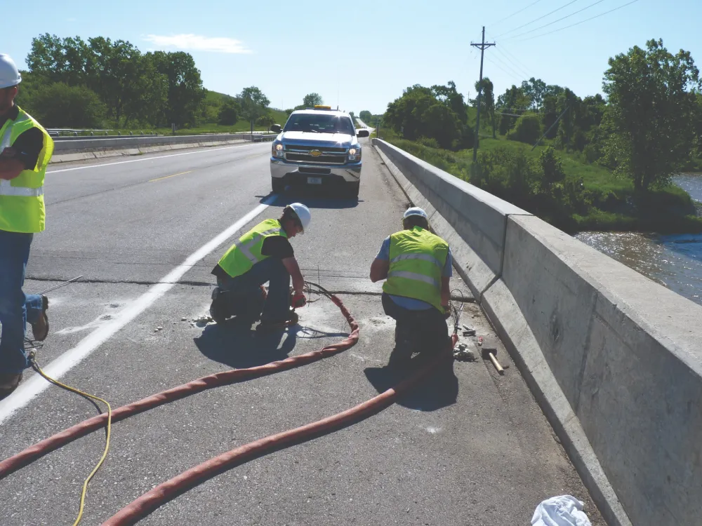 Workers repairing bridge roadway under sunny conditions.