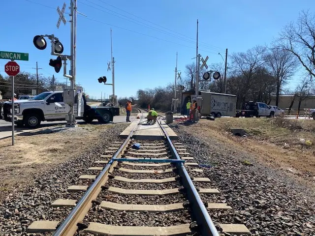 Workers maintaining railroad tracks during sunny day.