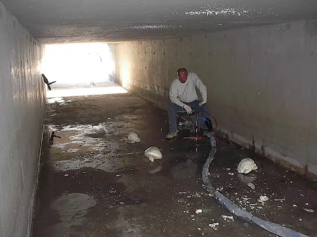 Man with equipment in a concrete tunnel.