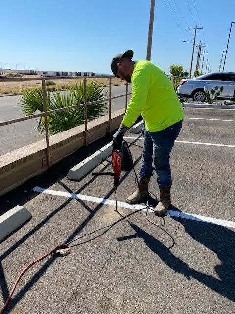 Worker using jackhammer on parking lot pavement.