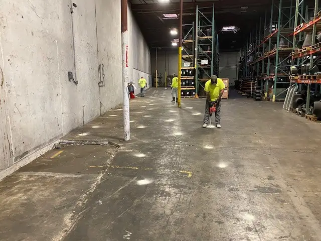 Workers in yellow safety vests polylift injection on warehouse floor.