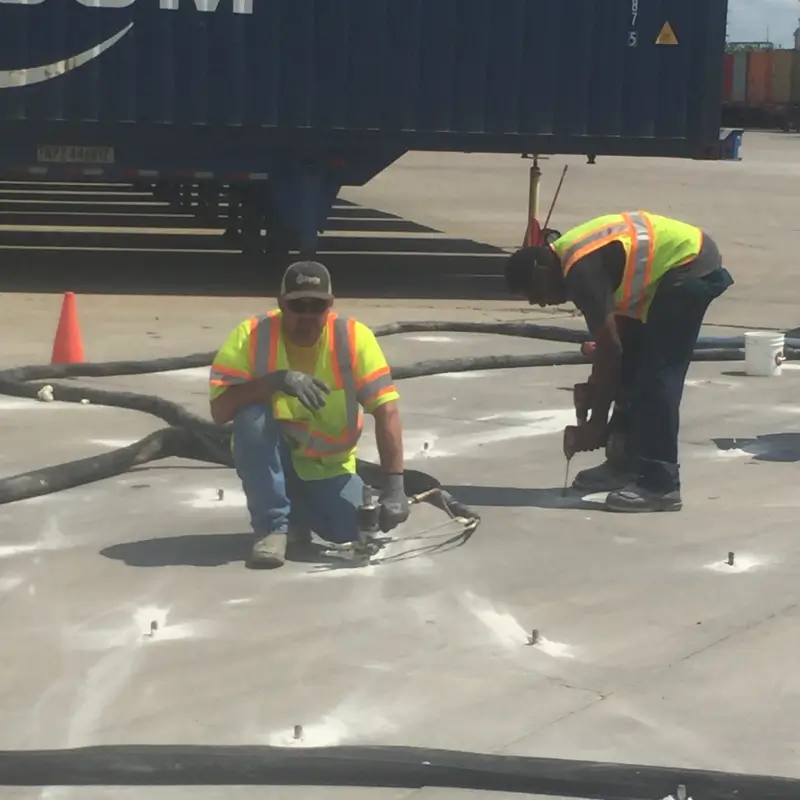 Workers in hi-vis repairing warehouse floor with tools.