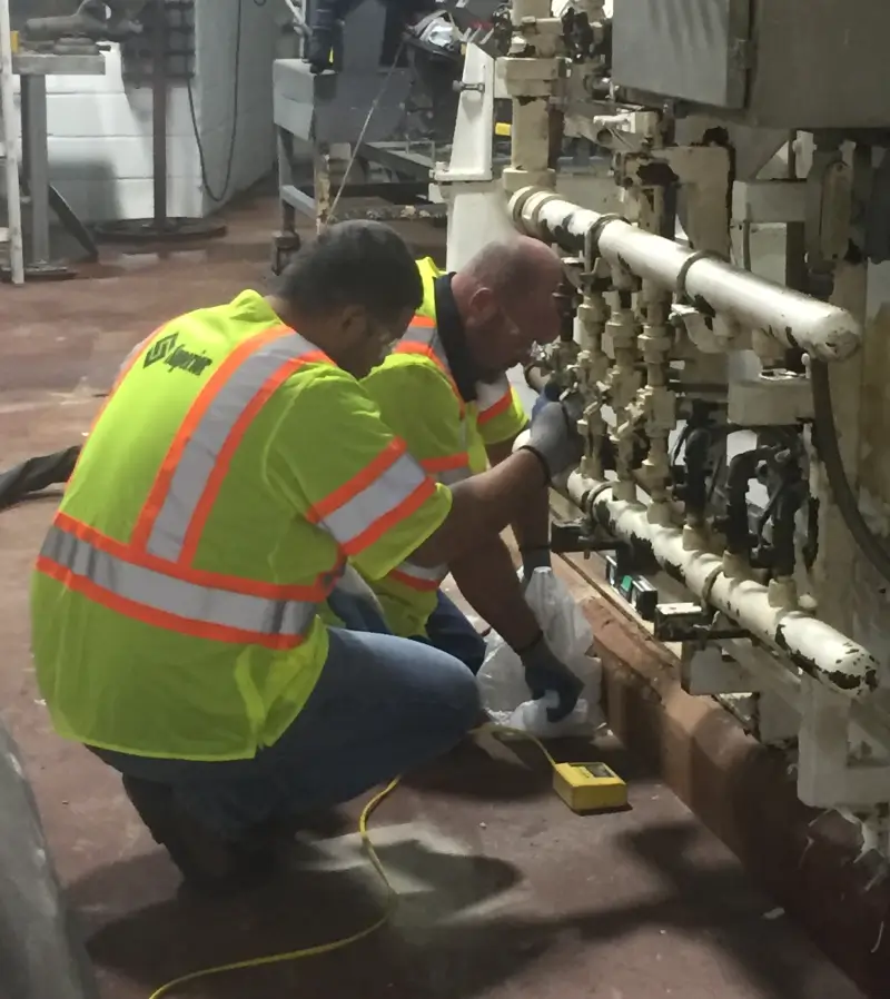 Two technicians repairing machinery in industrial setting.